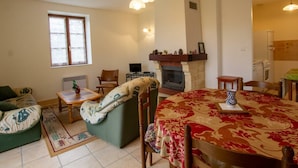 A cozy living room with a fireplace, a dining table with a patterned tablecloth, and a comfortable seating area with a sofa and chairs. - Charming Quiet House Near Sarlat with Fireplace and Terrace (Tursac)