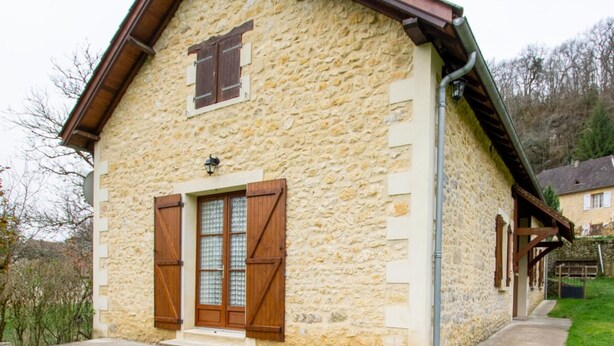 A stone building with a wooden door and shutters, a small porch, and a grassy yard. - Charming Quiet House Near Sarlat with Fireplace and Terrace (Tursac)