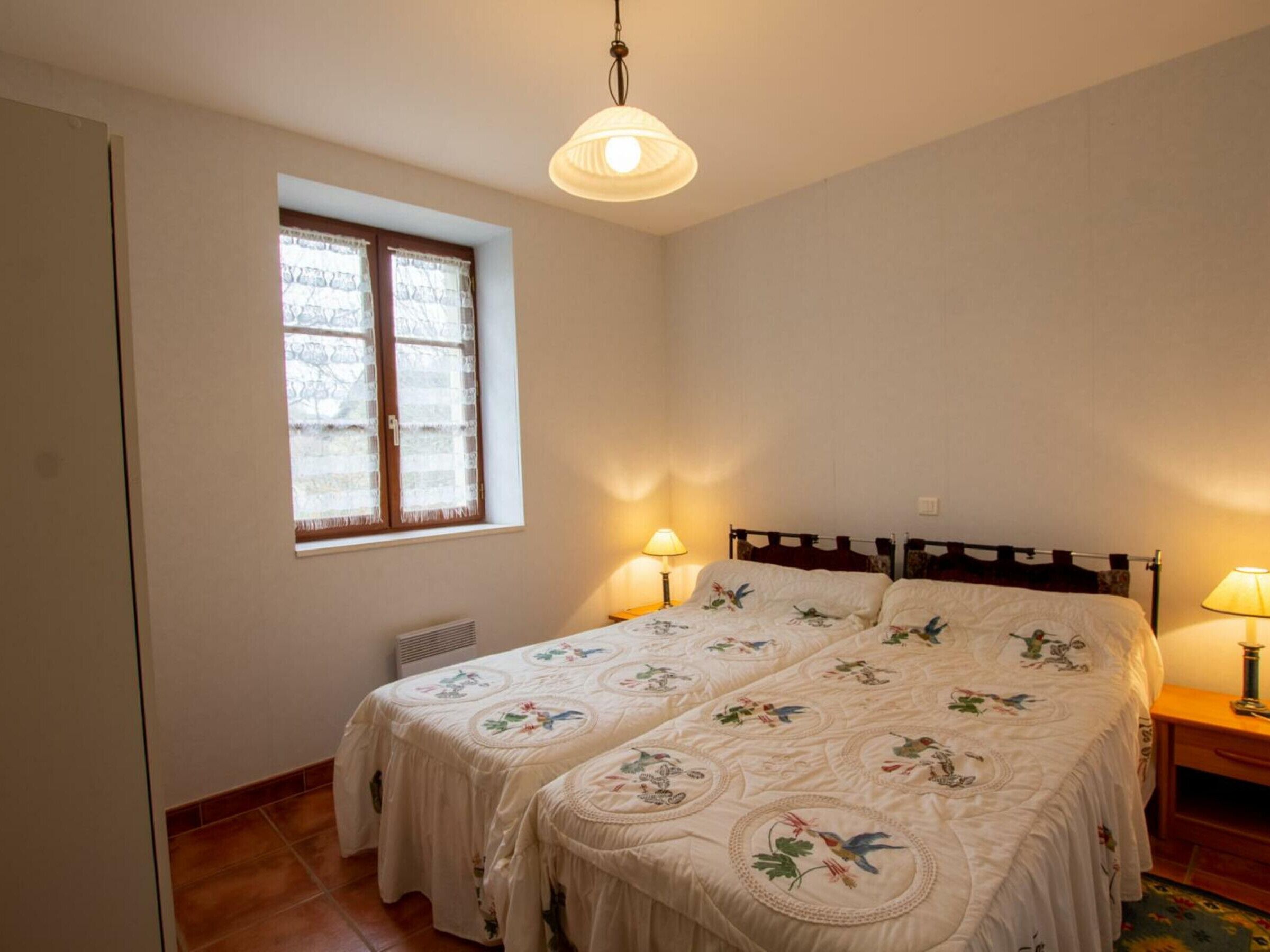 Un dormitorio con dos camas, una ventana con cortinas, una lámpara colgante y una mesita de noche con lámpara.