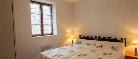 Un dormitorio con dos camas, una ventana con cortinas, una lámpara colgante y una mesita de noche con lámpara.