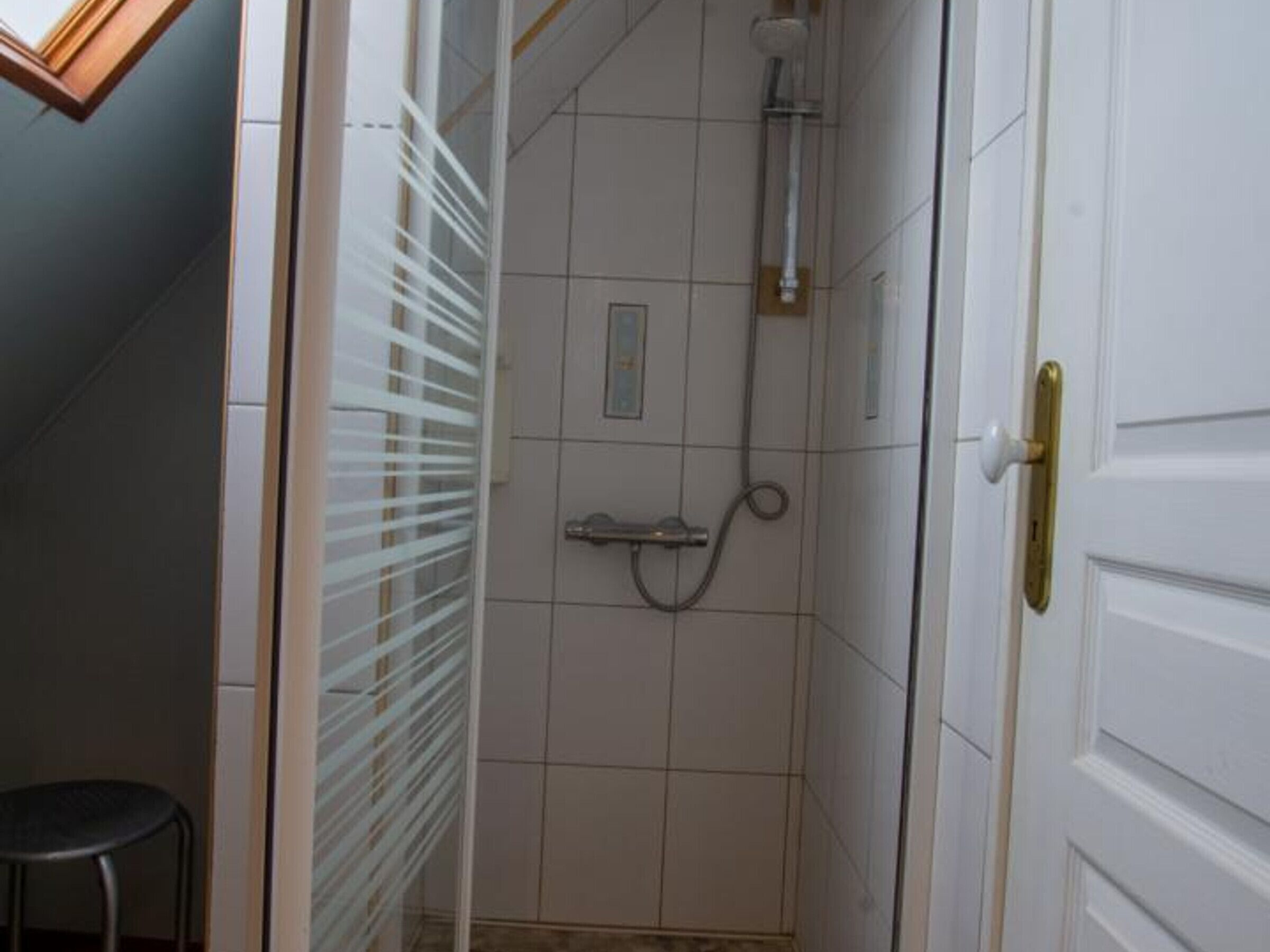 Piccola cabina doccia con piastrelle bianche, soffione e doccetta a mano.