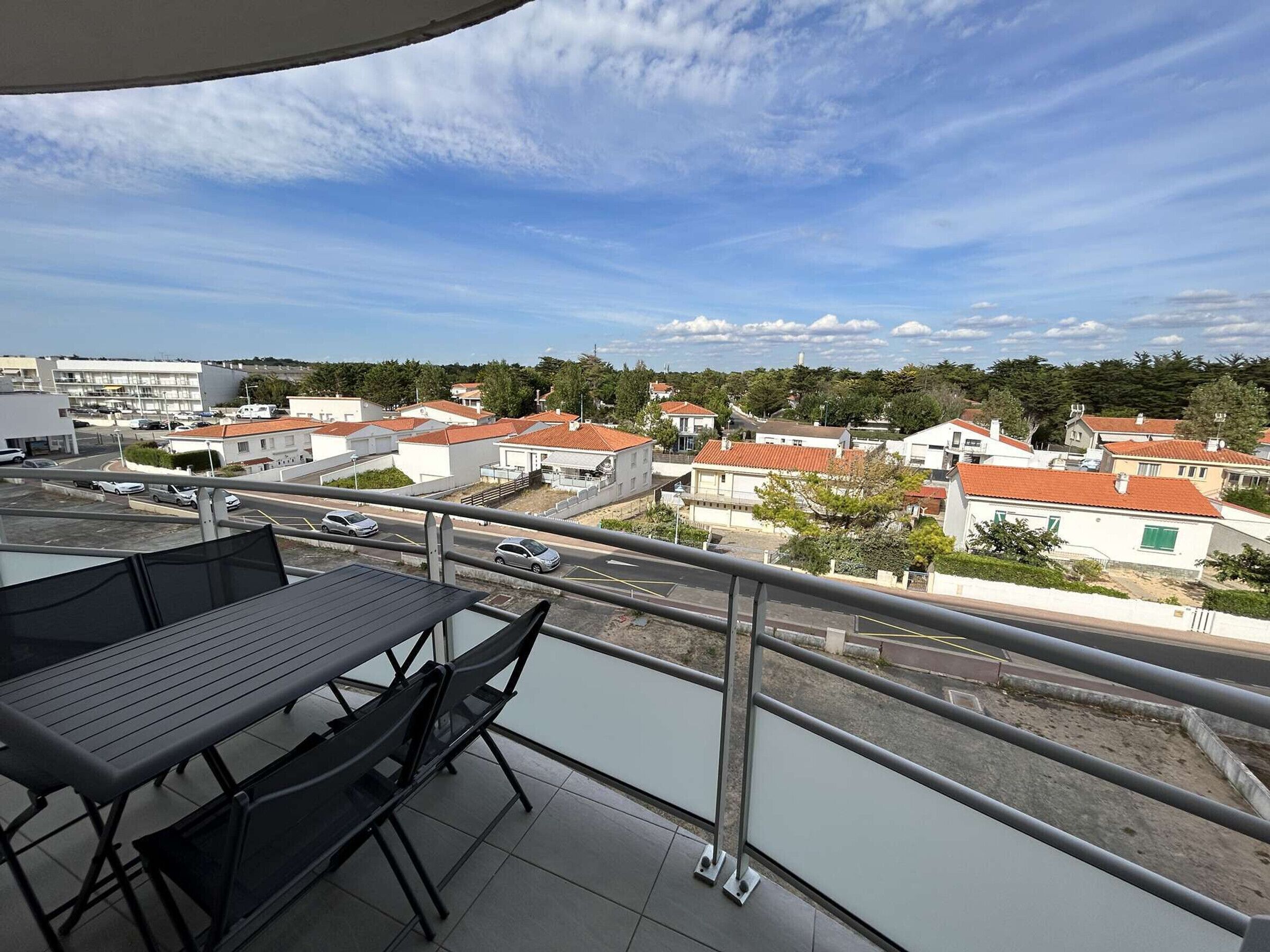 A balcony with a table and chairs, overlooking a residential area with houses and a road.