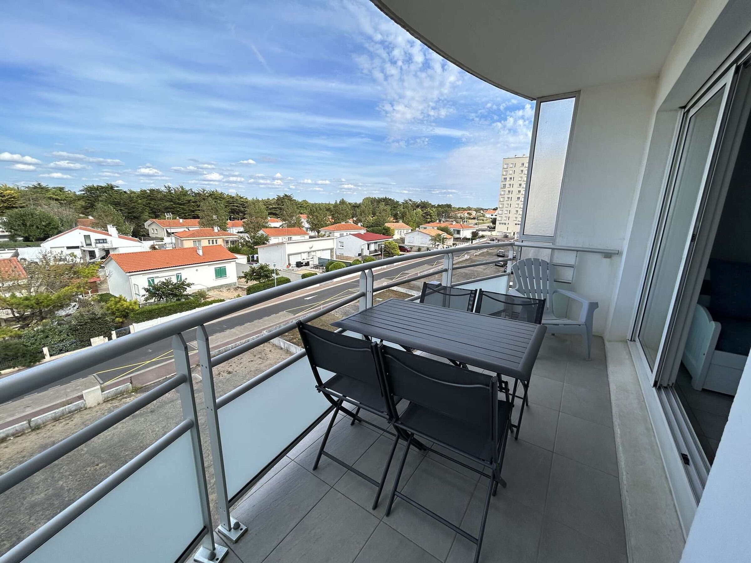A balcony with a table and chairs, overlooking a residential area with houses and a road.