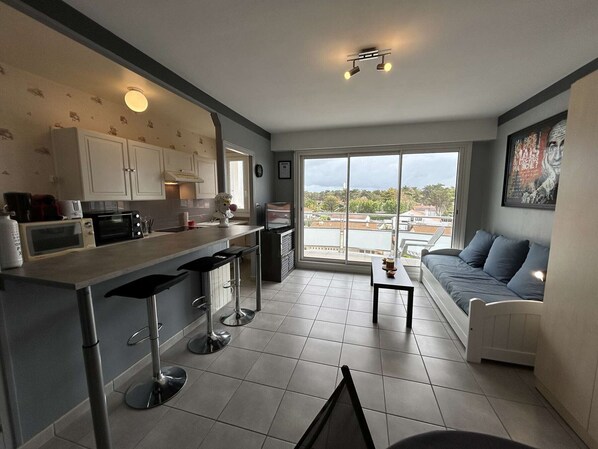 Un apartamento moderno con cocina, comedor y sala de estar. Cuenta con un amplio ventanal con vista a la ciudad, un sofá y una pequeña mesa.