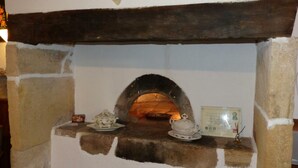 A stone-built fireplace with a wooden mantel, a small shelf with decorative items, and a framed certificate on the wall.