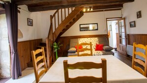 A rustic dining area with a wooden table and chairs, a staircase, and a cozy seating area with cushions.