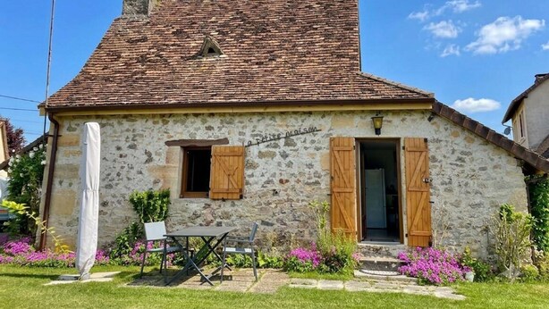A stone house with a tiled roof, wooden shutters, and a small garden with flowers.
