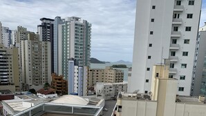 A rooftop pool area with a hot tub and a standard pool, surrounded by high-rise buildings and a view of the sea.
