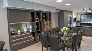 A modern dining area with a glass table surrounded by dark chairs, a built-in shelving unit with decorative items, and a kitchen in the background.