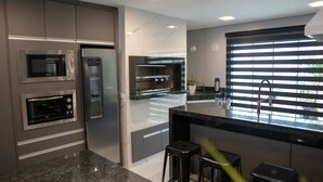 A modern kitchen with built-in appliances, a large window with blinds, and a bar area with stools.