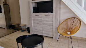 Ein modernes Wohnzimmer mit einem Holzkabinett, einem schwarzen Fernseher, einem runden schwarzen Tisch und einem gelben Korbstuhl.