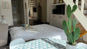 Ein Schlafzimmer mit einem Bett, einem Sessel, einem Tisch und einer Kakteenpflanze.