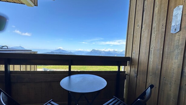 Une terrasse en bois avec une table ronde et deux chaises, offrant une vue sur un paysage montagneux.