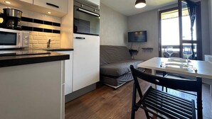 Une cuisine compacte équipée d’un four à micro-ondes, d’une cuisinière et de meubles de rangement modernes. On y trouve également un coin repas avec une table et des chaises, ainsi qu’un téléviseur fixé au mur.