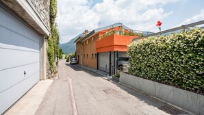 A narrow street with a parked car, a building with a garage, and a hedge with a flag. - GuestHost - Bright and welcoming studio apartment located in Cernobbio in an elevated position, in a hilly and residential area of the village! The apartment boasts a truly superb lake view: you can admire a unique panorama, which ranges from the swimmin (Cernobbio)