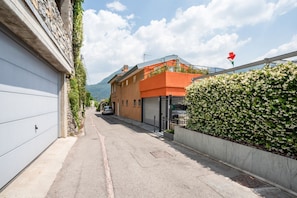 Una stretta via con un'auto parcheggiata, un edificio con un garage e un siepe con una bandiera.