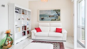 A living room with a white sofa, a bookshelf, a painting, and a chandelier. - GuestHost - Bright and welcoming studio apartment located in Cernobbio in an elevated position, in a hilly and residential area of the village! The apartment boasts a truly superb lake view: you can admire a unique panorama, which ranges from the swimmin (Cernobbio)