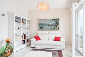 Un soggiorno con un divano bianco, una libreria, un quadro e un lampadario.