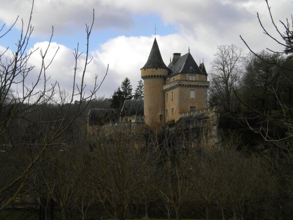 A castle with multiple towers, surrounded by trees and a cloudy sky.