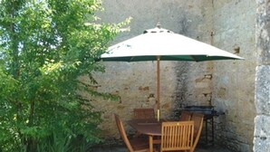 An outdoor patio with a table and chairs, a green umbrella, and a stone wall. - Charming village house near Villefranche du Périgord, pets allowed, internet included (Loubejac)