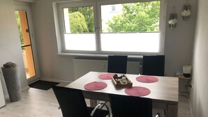 Et spiseområde med et bord dækket til fire personer, sorte stole og et vindue med udsigt til grønne omgivelser.