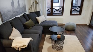 Un salon moderne avec un canapé d’angle foncé, une table basse ronde noire et un tapis beige.