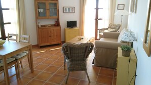 A living room with a sofa, a dining table with chairs, a television, and a cabinet with glass doors.