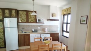 A compact kitchen with a refrigerator, microwave, sink, and a dining area with a table and chairs.