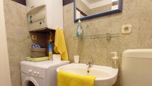 A compact bathroom with a washing machine, a sink, a toilet, and a mirror. - Holiday apartment Lungomare, only 300m from the beach (Pula)