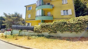 A multi-story yellow building with balconies, a covered outdoor area, and a hedge in front. - Holiday apartment Lungomare, only 300m from the beach (Pula)