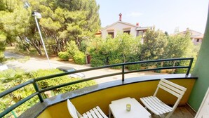 A balcony with two white plastic chairs and a small table, surrounded by yellow walls and a green railing. - Holiday apartment Lungomare, only 300m from the beach (Pula)