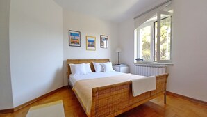 A bedroom with a wooden bed, white bedding, a bedside table with a lamp, and a window with a view of trees. - Holiday apartment Lungomare, only 300m from the beach (Pula)