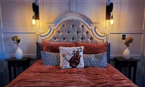 A bed with a tufted headboard, two bedside tables with vases, and wall-mounted light fixtures.