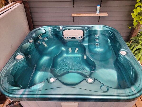 Un bain à remous de spa doté d’un panneau de commande, entouré d’une terrasse en bois et de plantes.