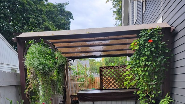 Eine Holzterrasse mit einer Bank, einem Whirlpool und einem mit Grünwerk bewachsenen Pergola.