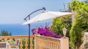 Una terraza con sombrilla blanca, mobiliario exterior y vistas al mar.