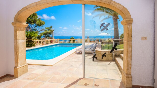 Puerta de vidrio que da a una zona de piscina con vistas claras al mar y palmeras.