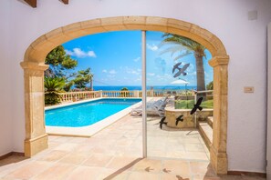 Une porte vitrée donne accès à un espace piscine d’où l’on a une vue dégagée sur la mer et les palmiers.