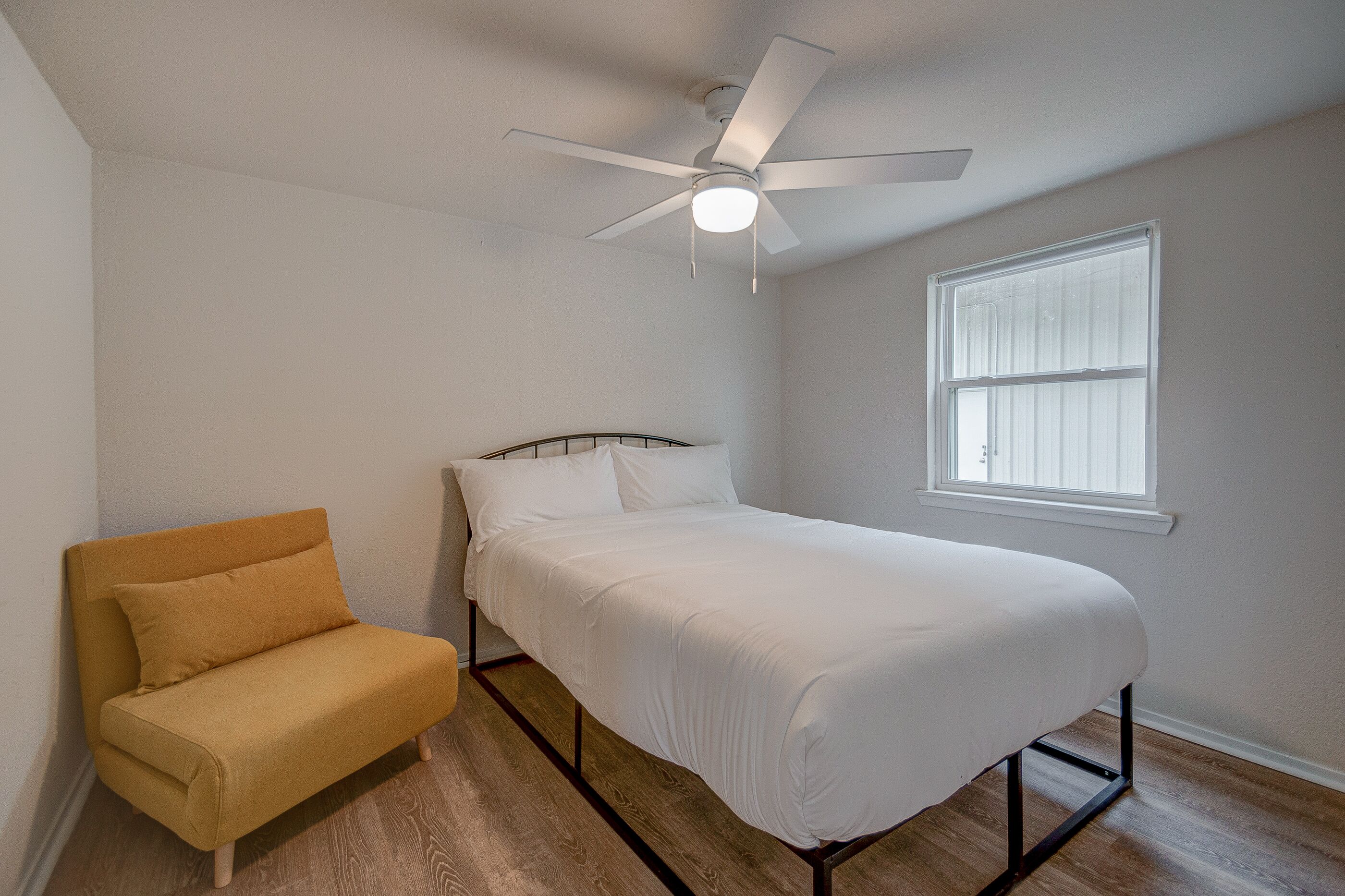 Ein Schlafzimmer mit einem Bett, einer Couch, einem Deckenventilator und einem Fenster.