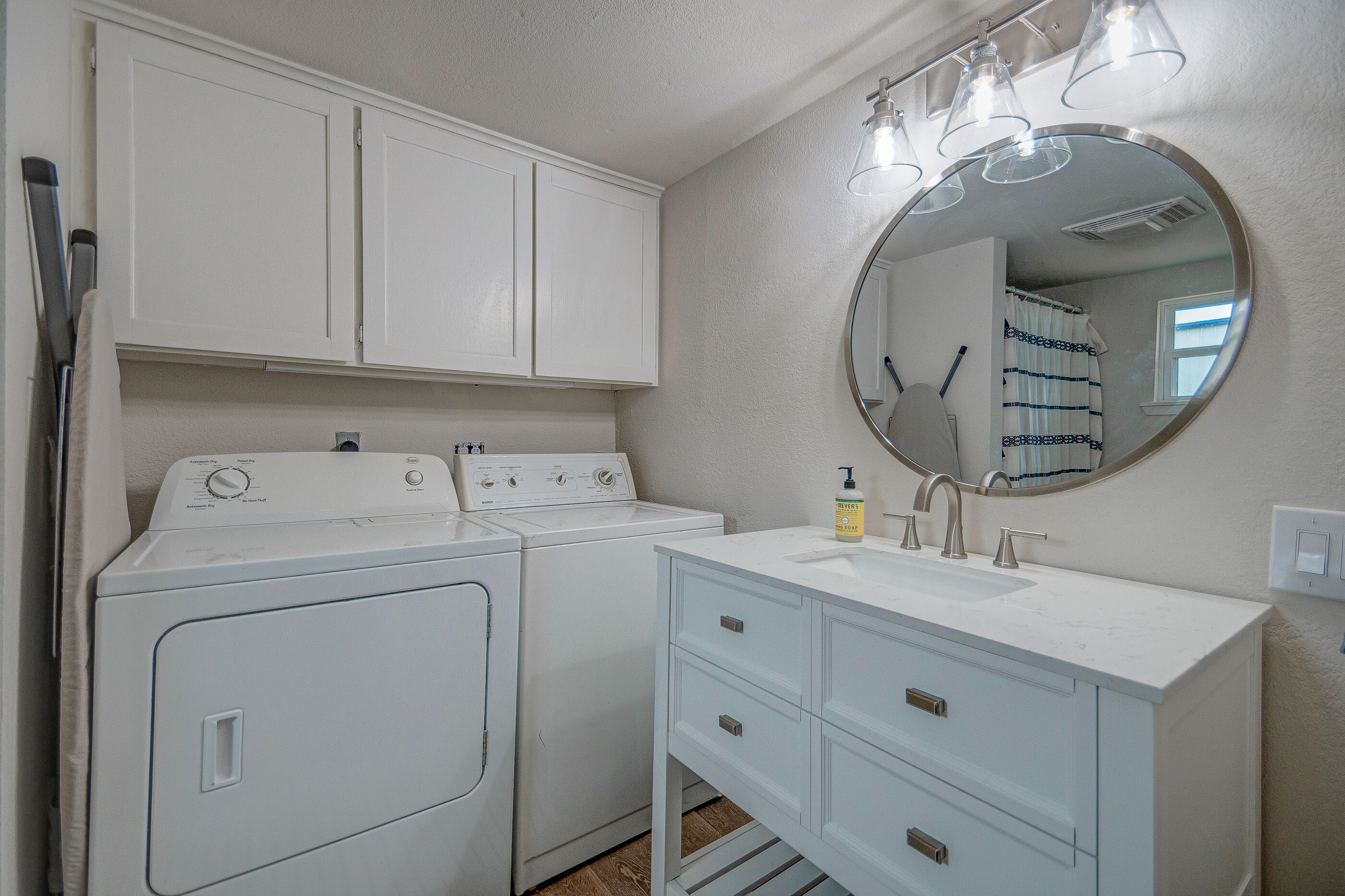 A laundry area with a washing machine and dryer, a sink with a mirror, and a window with curtains.