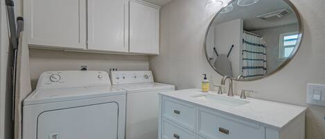 A laundry area with a washing machine and dryer, a sink with a mirror, and a window with curtains.