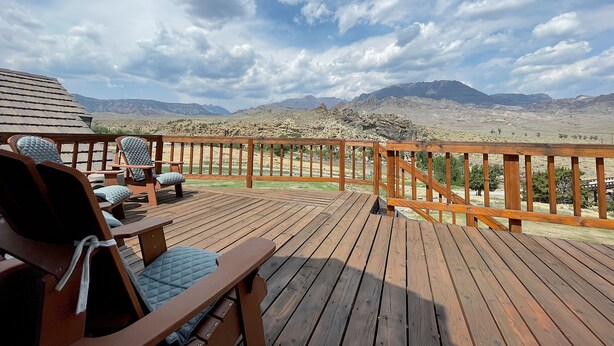 A wooden deck with chairs and a table, overlooking a mountainous landscape. - Studio 57- luxury apartment in the Wapiti Area! (Cody)