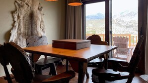 A wooden dining table with chairs, a rustic wall, and a view of mountains through a large window. - Studio 57- luxury apartment in the Wapiti Area! (Cody)
