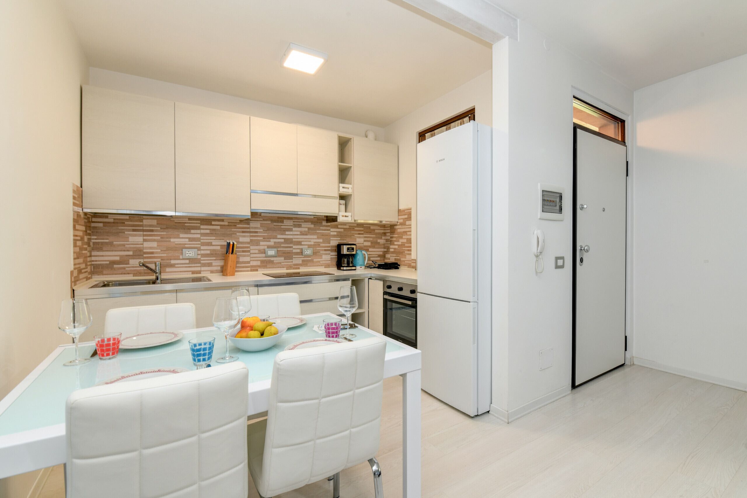A modern kitchen with white cabinets, a tiled backsplash, and a dining area with a table set for two.