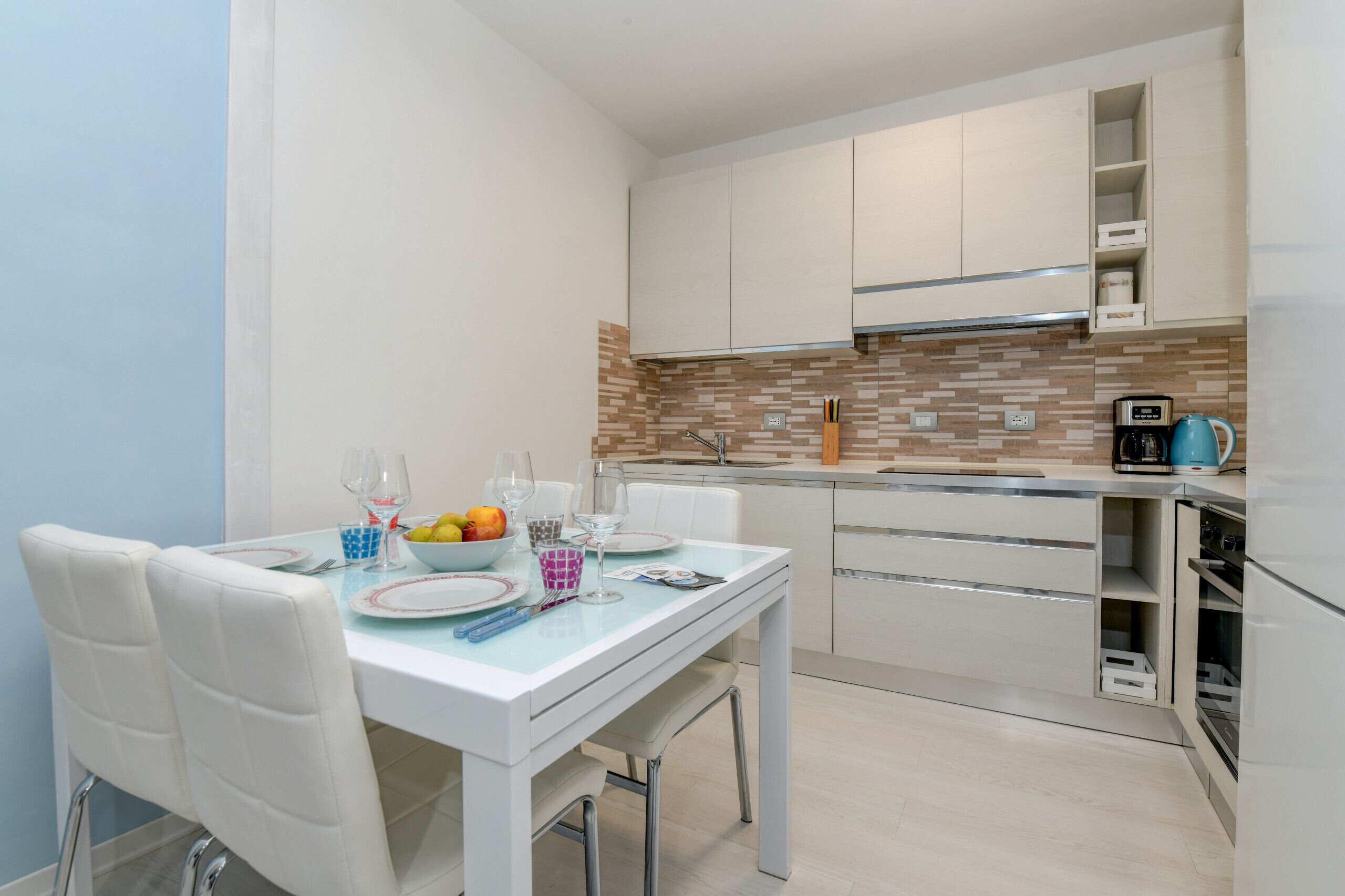 Eine moderne Küche mit weißen Schränken, einer gefliesten Spritzschutzwand und einem Essbereich mit Tisch für Zwei.