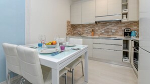 Eine moderne Küche mit weißen Schränken, einer gefliesten Spritzschutzwand und einem Essbereich mit Tisch für Zwei.