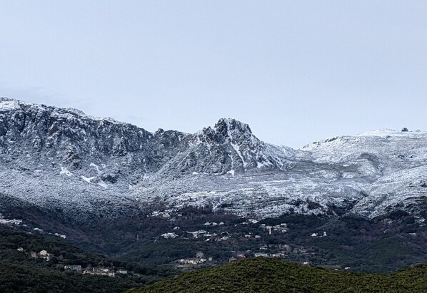 A mountainous landscape with snow-covered peaks and a valley with scattered buildings. - Dans LE CAP Corse,rez-de-chaussee DE Villa, Jardin Privatif, VUE Mer/ Montagne (Sisco)