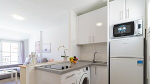 A compact kitchen with a built-in washing machine, a microwave, and a refrigerator. - Modern Apartment with pool in El Castillo - Home For Guest (Antigua - Fuerteventura)