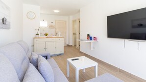A modern living room with a grey sofa, a white coffee table, and a flat-screen TV mounted on the wall. - Modern Apartment with pool in El Castillo - Home For Guest (Antigua - Fuerteventura)