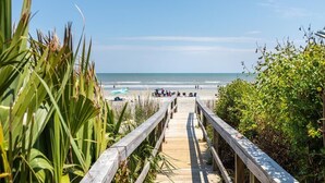 A wooden boardwalk leading to a beach with people in the distance. - Oceanfront Luxury Home with Large Deck & Direct Beach Access - No Egrets (Folly Beach)